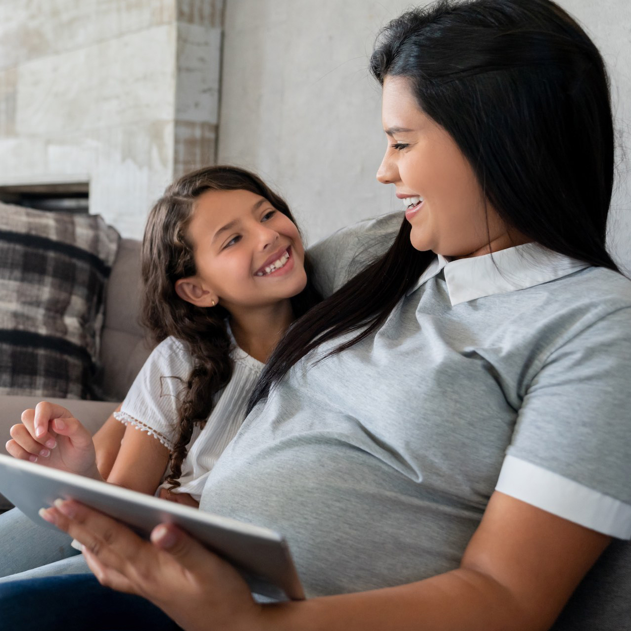 Pregnant mother and daughter talking while using a tablet.