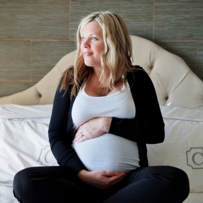 Pregnant mother holding her belly while sitting on a bed
